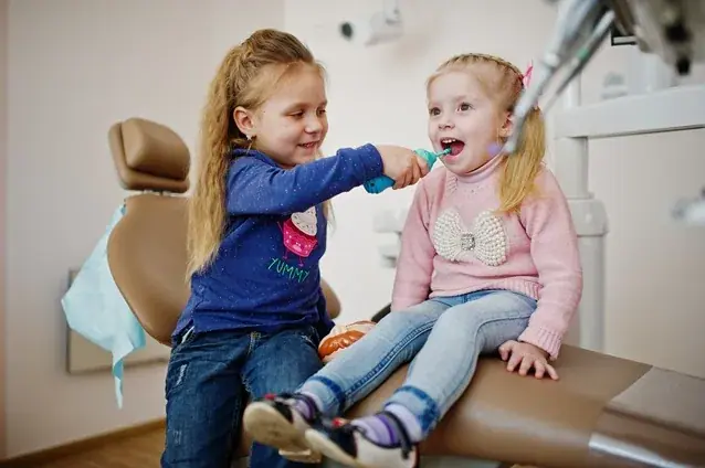 Hai bé gái vui vẻ chơi trên ghế nha khoa trẻ em tại Texas Dental Center ở Houston.